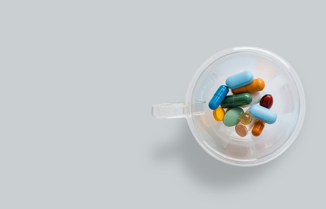A transparent coffee cup with colourful pills on gray background.